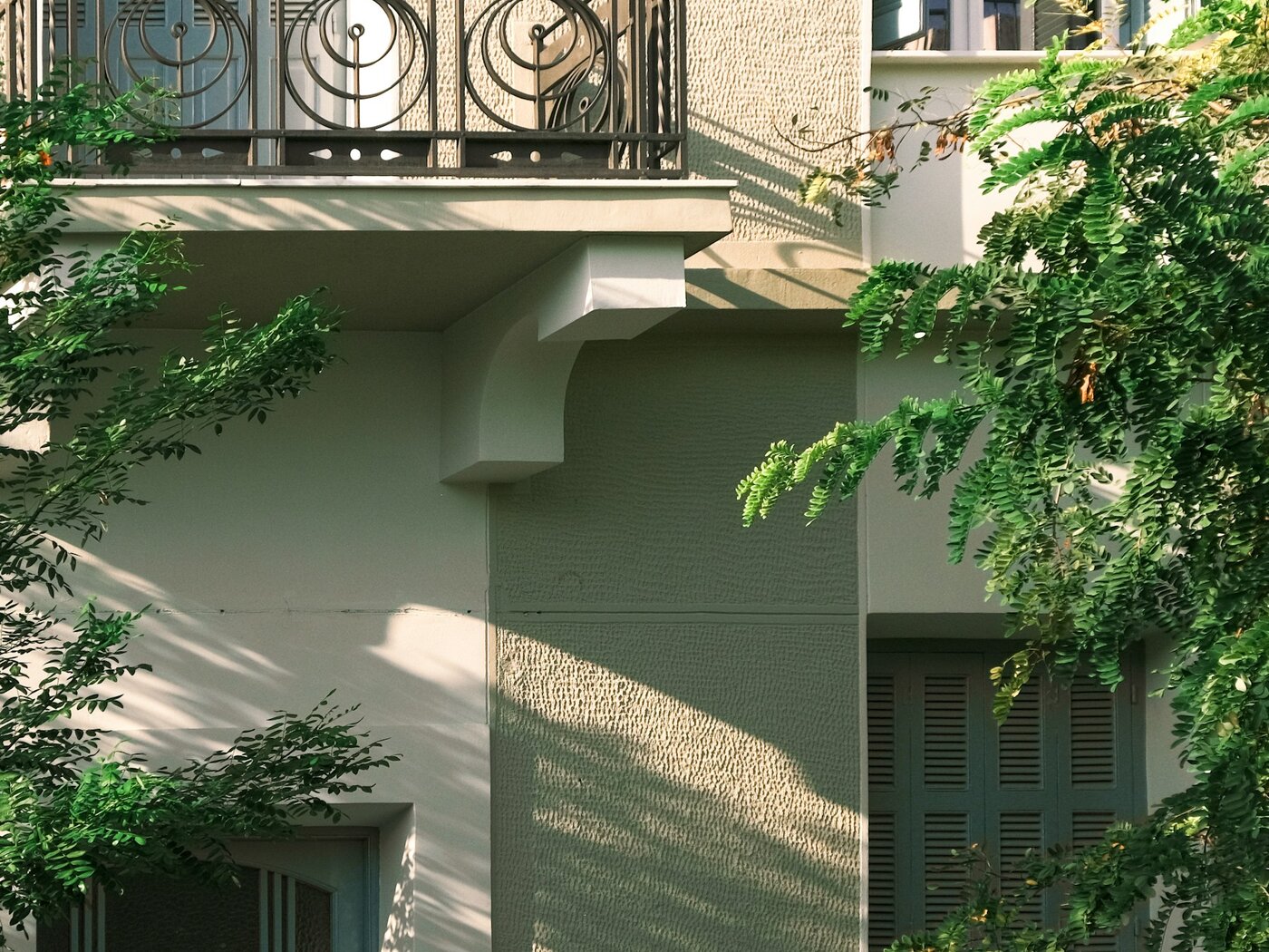Greek residential facade with green shutters, wrought-iron balconies and leafy trees