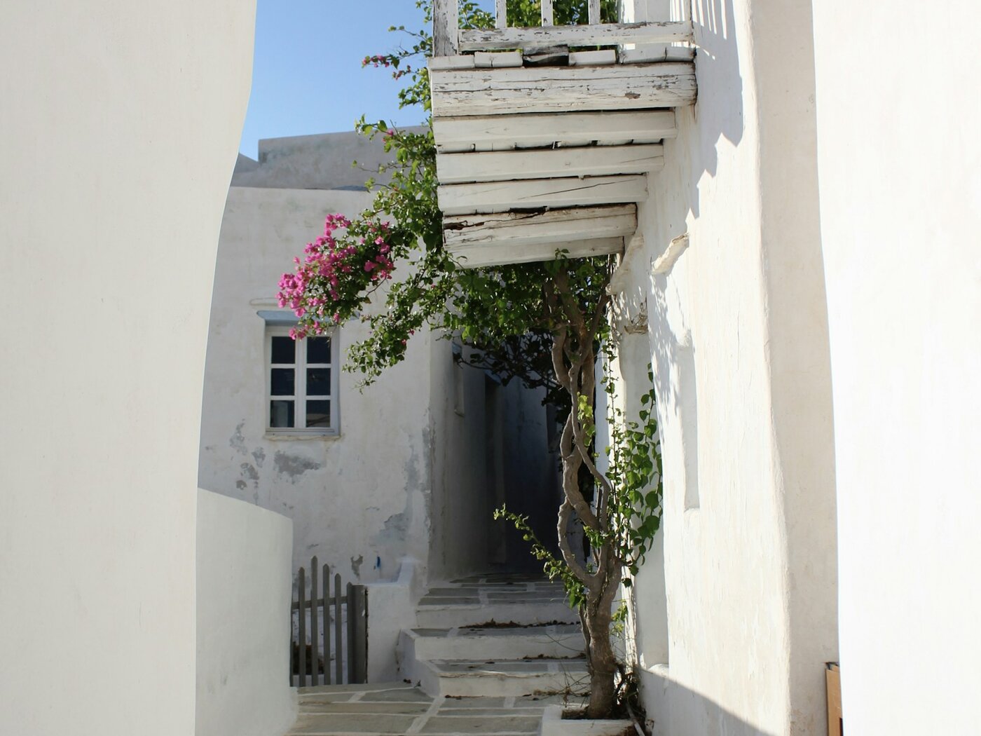 Whitewashed Greek island homes beside a stone lane, with a wooden balcony and flowering plants