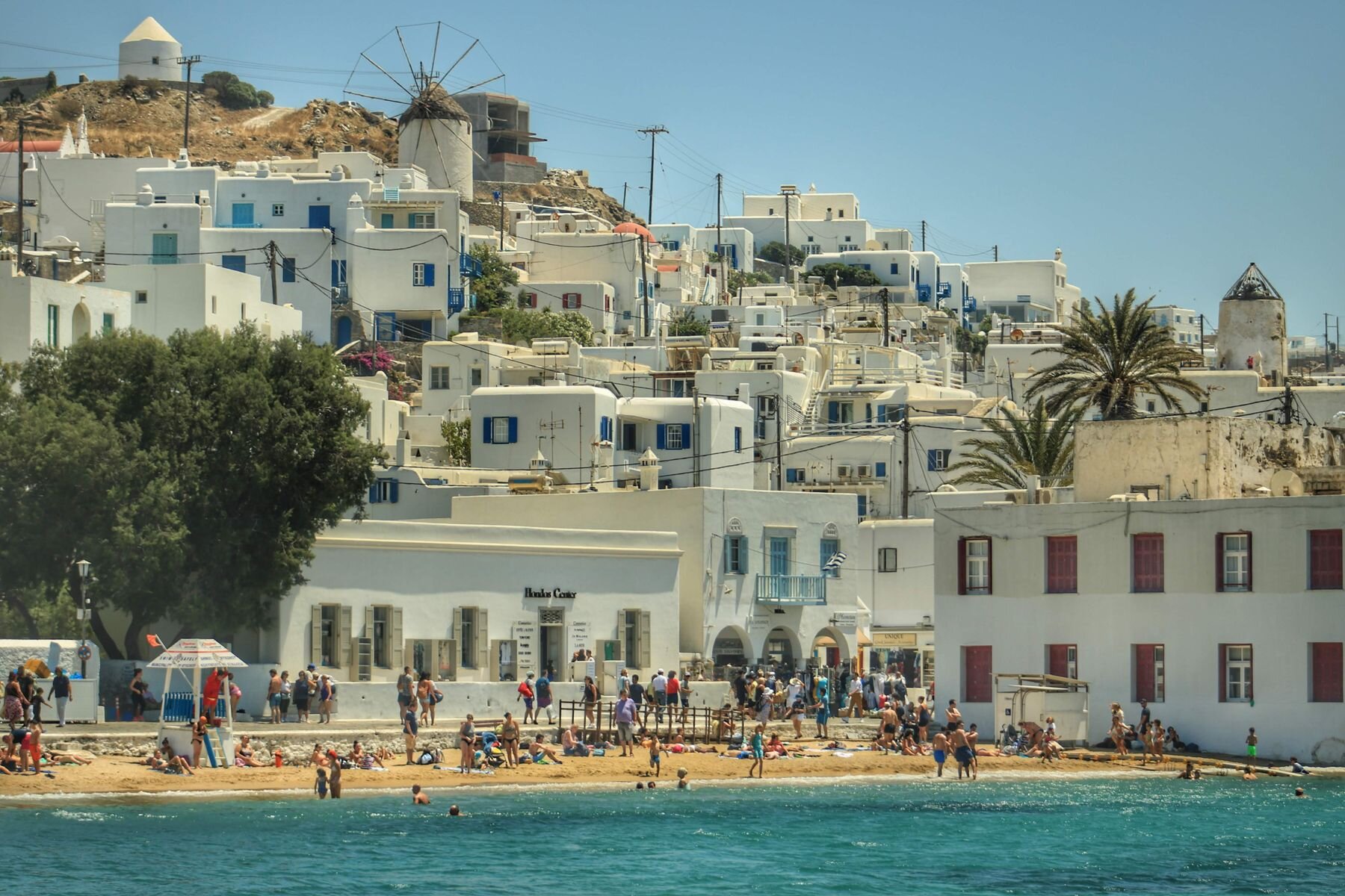 Whitewashed Mykonos buildings beside a small beach and clear sea